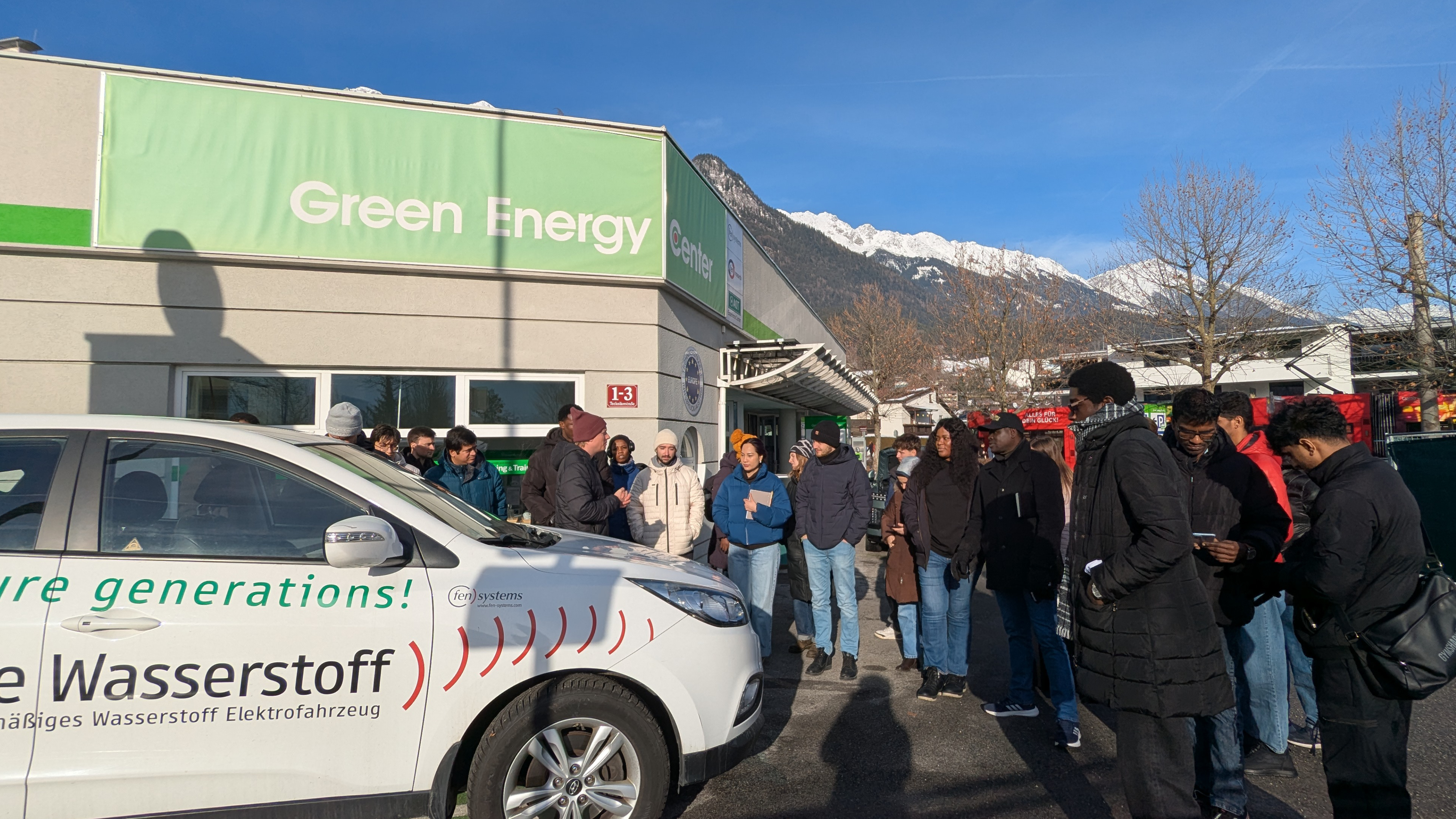 Students standing outside as Nicolas Fleischhacker explains green energy car charging, viewed from the other side with the car door closed